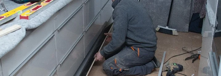 Person verlegt Fußbodenleiste in Küche